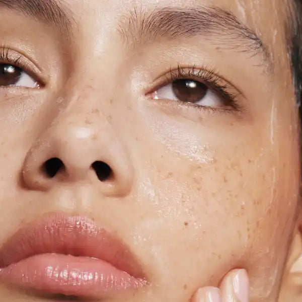 Close-up beauty shot showing freckled skin, glossy lips, and warm brown eyes.