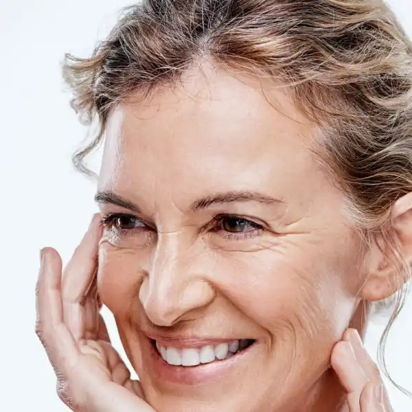 A close-up portrait showing a bright, genuine smile and gentle touch to the face.