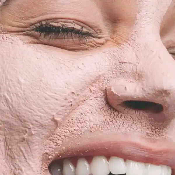 Close-up view of a face wearing a pink clay face mask while smiling.