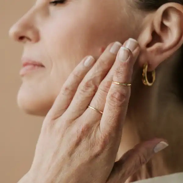 Delicate hand wearing multiple thin gold rings touching the side of a face.