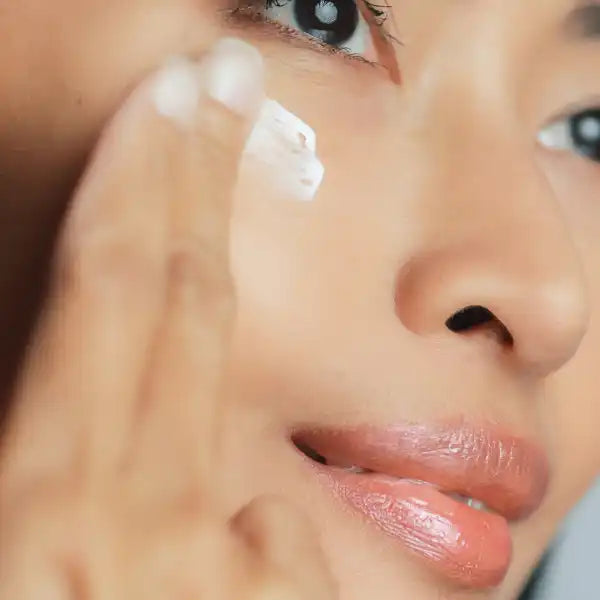 A finger applying white moisturizer or skincare cream to the face.