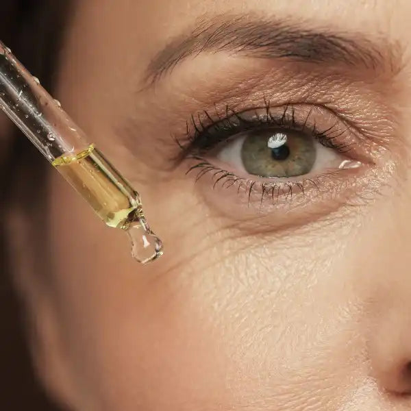 Glass dropper containing golden-colored serum or oil near an eye.