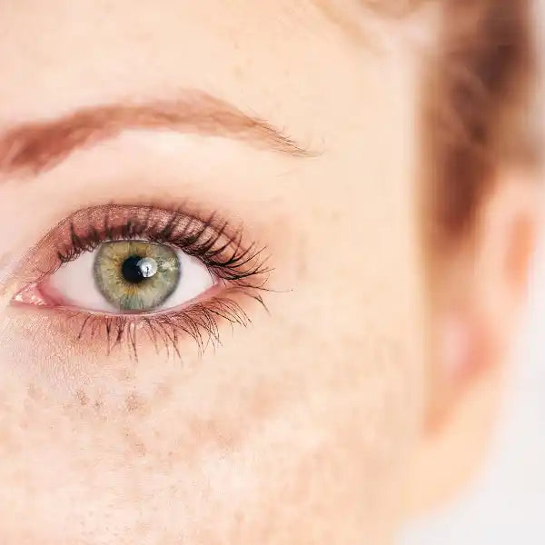 A green-hazel eye with long eyelashes and a defined eyebrow.