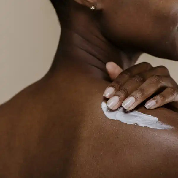 Hand with white nail polish applying moisturizer or lotion to dark skin.