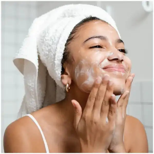 Person wearing a white towel on their head while applying facial cleanser.